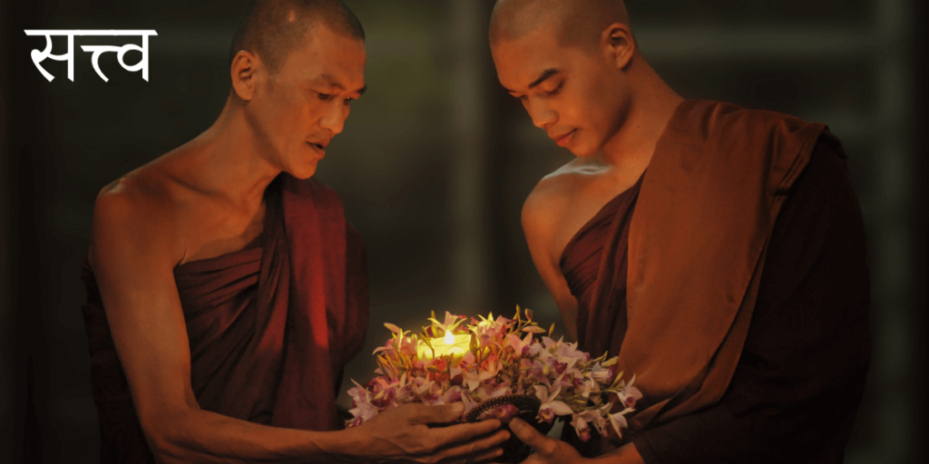 2 moines tiennent un panier de fleurs avec une bougie allumée au centre avec le titre en Sanskrit Satva