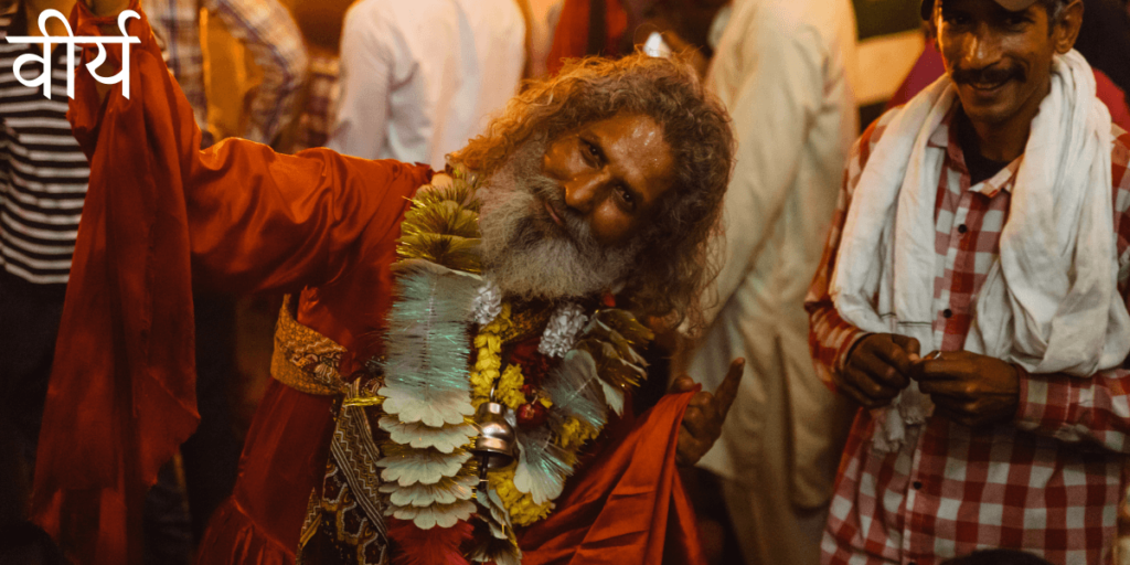 un joyeux saddhu indien habillé en rouge incline la tête sur le côté et lève la main en signe de reconnaissance avec le titre un Sanskrit Virya