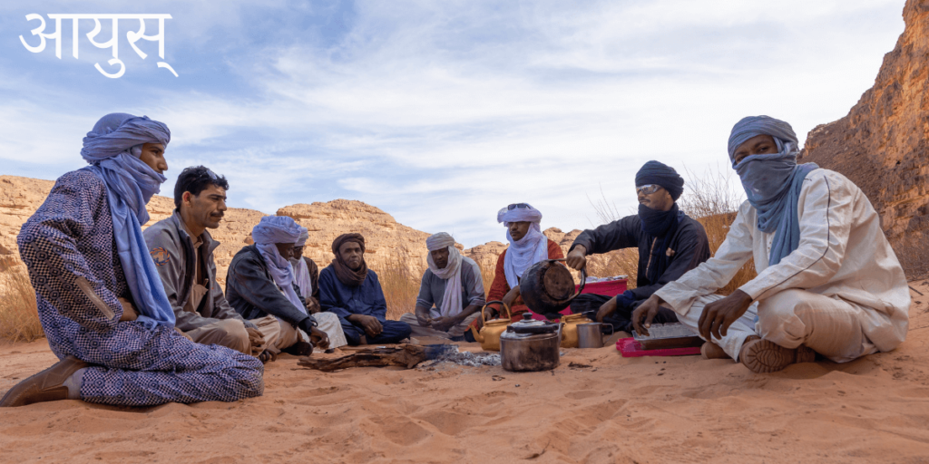 8 hommes dans le désert assis pour prendre une infusion de thé à la menthe avec le titre sanskrit आयुस्-Ayu