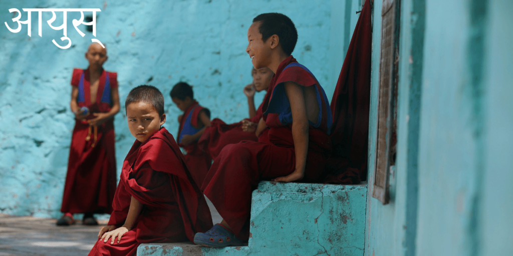 Des enfants dans un monastère bouddhiste assis sur des marches avec le titre sanskrit हिम-ayu avec